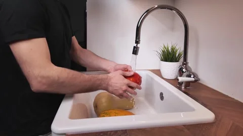 Man washing pumpkin under tap water in kitchen sink Video stock 330899532