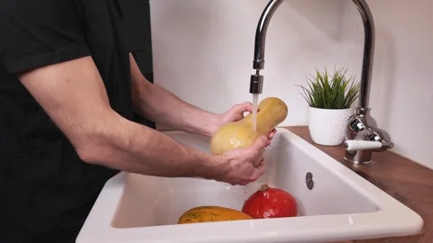 Man washing pumpkins in kitchen sink under running water Video stock 330898301