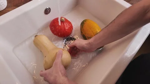 Man washing two pumpkins in kitchen sink, high angle view Video stock 330899147