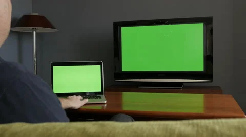 Man watching and cheering in front of laptop and tv, both with green screen Stock Footage 54029695