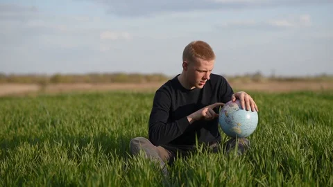 Man watching earth globe while sitting in green field Stock Footage 129082233