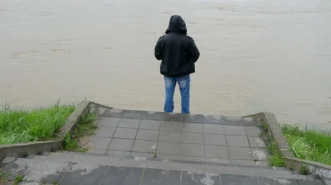The man watching flooded river flow from stairs tilt up to the wide angle view. Video stock 62959208