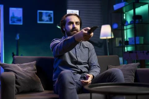 Man watching shows on TV, using remote control, picking what movie to watch next Fotos de archivo