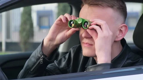 A man is watching someone with binoculars while sitting in a car Stock Footage 152982950