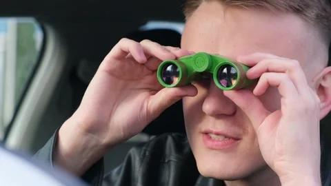 A man is watching someone with binoculars while sitting in a car 库存影片 152983315