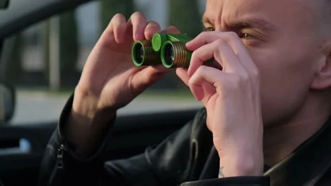 A man is watching someone with binoculars while sitting in a car Stock Footage 152983454