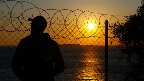Man watching sunset behind barbed wire fence Stock Footage 302816125