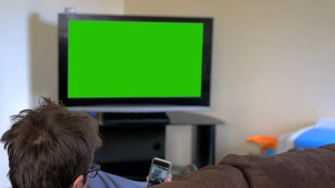 Man watching television and checking smart phone. Green screen and rear Video stock 93468616