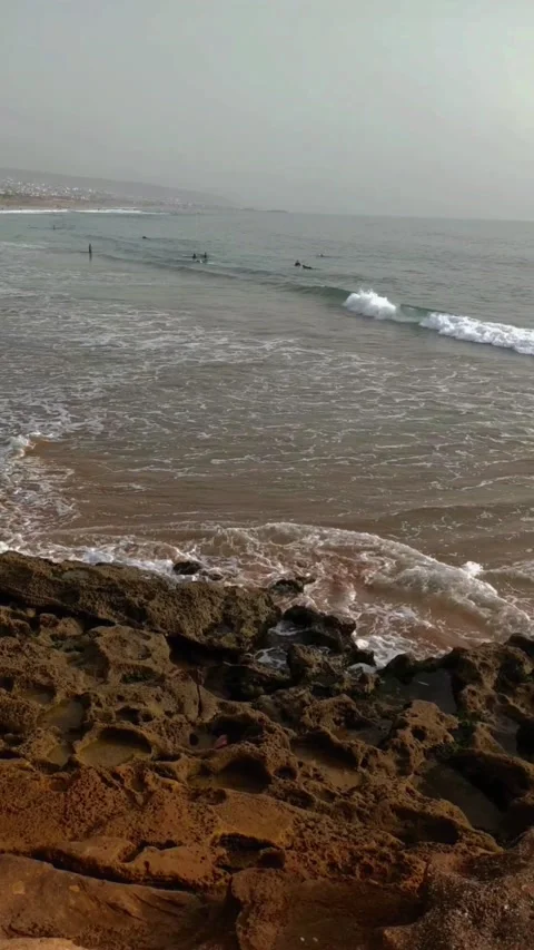 Man watching waves breaking on rocks with people doing surfing 库存影片 219356285