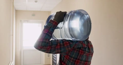 Man with water bottle walks down corridor of apartment building Stockbeeldmateriaal 294602222
