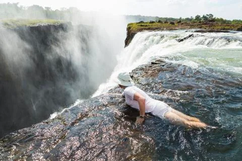 Man in the water at the Devils Pool on the edge of Victoria Falls, looking over Stock Photos