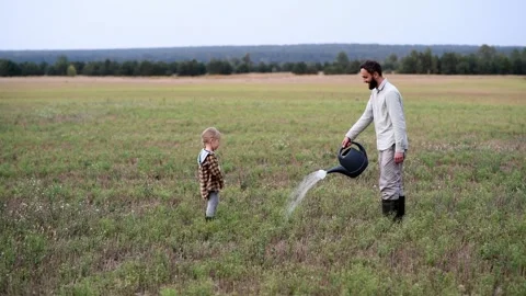 Man watering a field with a can while a little girl watches him attentively 库存影片 300096959