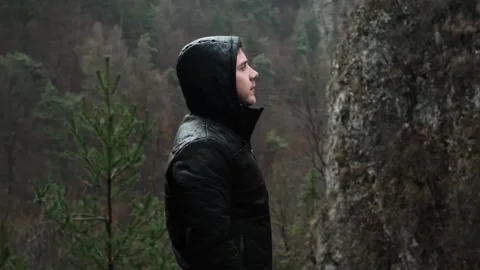 Man in a waterproof jacket stands on a cliff, enjoying a misty mountain view in Stock Footage 280186528