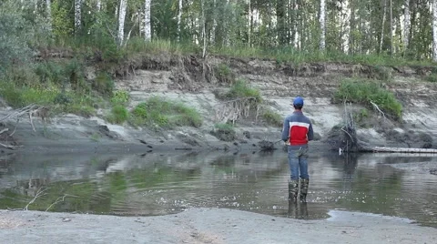 A man in waterproof overalls stands in a small river and spinning fishing. Stock Footage 54066786