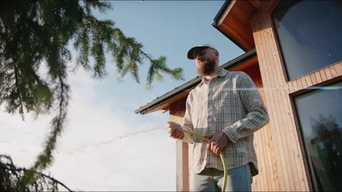Man waters plants and trees with a hose at summer sunset in the backyard Vídeo Stock 199870278