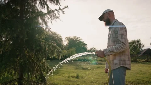 Man waters plants and trees with a hose at summer sunset in the backyard 스톡 동영상 199870896