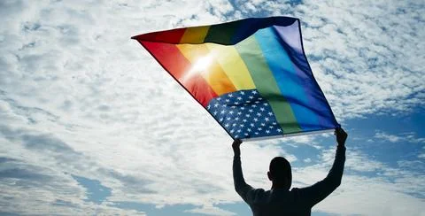 Man waves a rainbow US flag on the sky Stock Photos