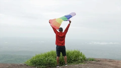 Man waving rainbow flag on mountain top slow motion shot Stock Footage 92156336