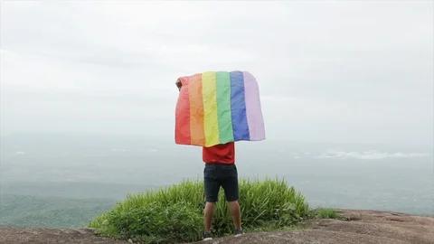 Man waving rainbow flag on mountain top slow motion shot Stock Footage 92159361