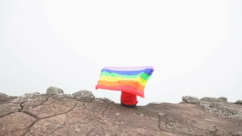 Man waving rainbow flag on mountain top Stock Footage 92251353