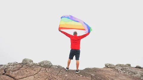 Man waving rainbow flag on mountain top Stock Footage 92251364