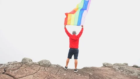 Man waving rainbow flag on mountain top Stock Footage 92252132