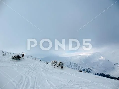 Man waving on white slope near icy bent tree. Ski trail and distant snowy mou Stock Photos