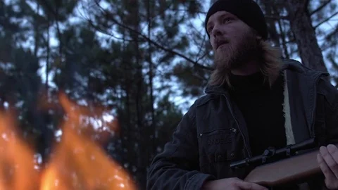 Man with a weapon warming in front of a campfire. Stock Footage 76477330