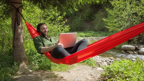 Man weared in casual lying in hammock at nature with laptop and talking by video Видео 132009354