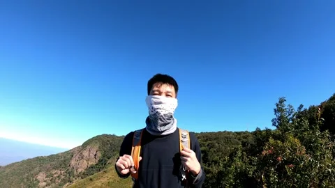 A man wearing a backpack and a scarf is standing on a hill Stock Footage 315930671