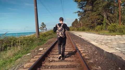 A man wearing a backpack walking along a train track in summer Stock Footage 110729148