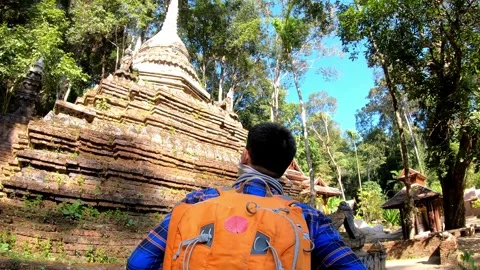 A man wearing a backpack is walking past a large stone building Stock Footage 314996181