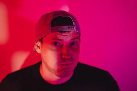 Man wearing baseball cap making silly face under pink neon lighting. Portrait Stock Photos