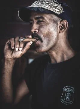 A man wearing a baseball cap smoking a cigar. Stock Photos