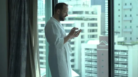 Man wearing bathrobe and browsing internet on tablet in hotel room Stock Footage 97725813