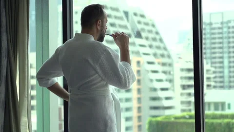 Man wearing bathrobe and brushing his teeth by the window, slow motion 240fps Stock Footage 97725142