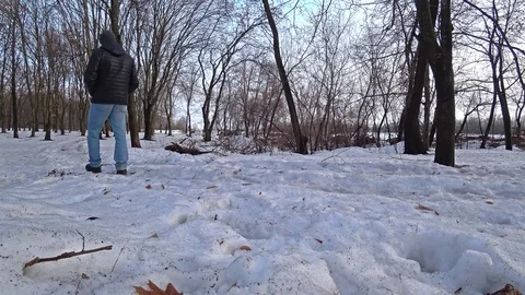 Man wearing a black jacket and blue jeans walking through a winter snow forest. Video stock 102396627