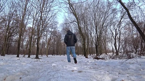 Man wearing a black jacket and blue jeans walking through a winter snow forest. Stock Footage 102396657