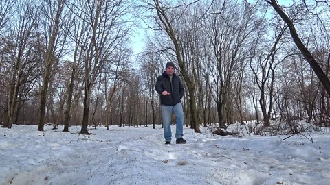 Man wearing a black jacket and blue jeans walking through a winter snow park. Stock Footage 102425673