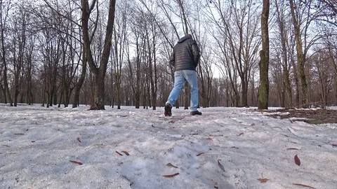 Man wearing a black jacket and blue jeans walking through a winter snow forest. Vídeo Stock 102425696