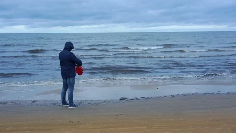 Man wearing blue jacket opens big red umbrella on seashore Stock Footage 120246186