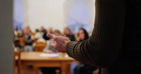 Man wearing brown turtleneck faces attentive crowd, delivering speech with Stock Footage 296326374