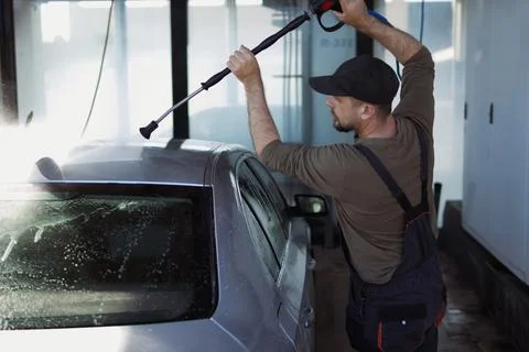 Man wearing a cap and work overalls using a pressure washer, cleaning a sil.. Stock Photos