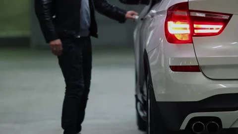 Man wearing dark clothes and white shoes gets in car on dark underground parking Stock Footage 276366243