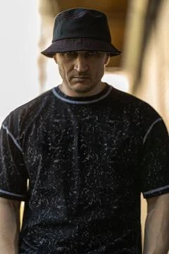 Man wearing a dark patterned t shirt and a bucket hat displays a serious Stock Photos