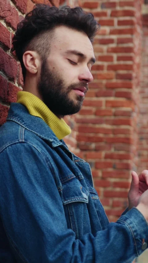 A man is wearing a denim jacket over a stylish green turtleneck, standing Stock Footage 314209931
