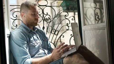 Man wearing earphones and having a videocall on modern notebook, steadycam shot Stock Footage