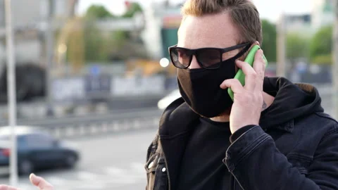Man wearing face mask, talking on the mobile phone and walking at the street. Video stock 129251909