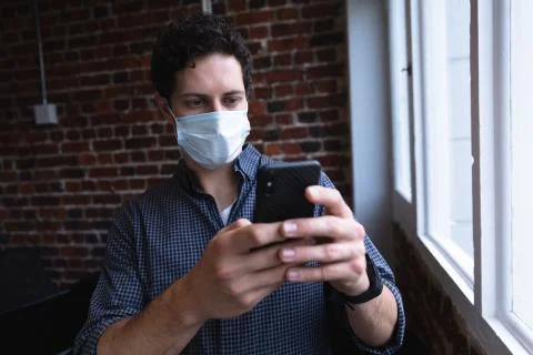 Man wearing face mask using smartphone at office Stock Photos
