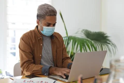 Man wearing face mask using laptop at office Photos